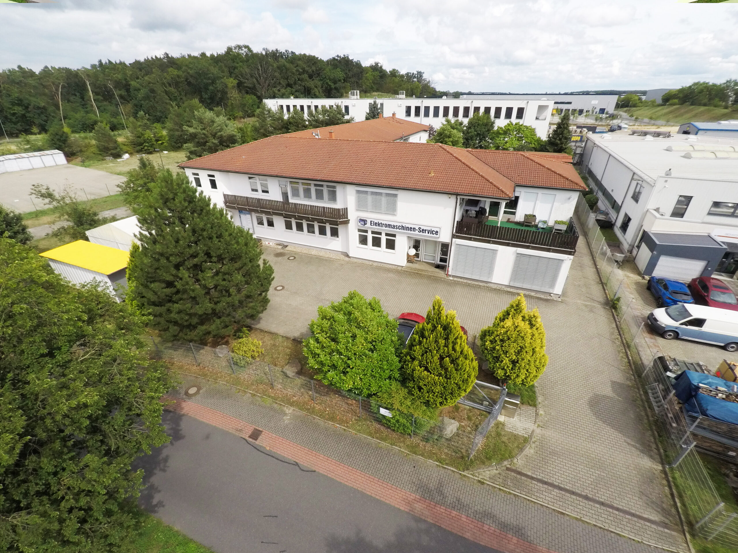 EMS Strzeletz Firmengebäude weiße Hausfarbe mit rotem Dach und Bäumen davor